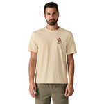 A man wearing the Patagonia men's balance organic top available at Babipur. A cream with short sleeves top showing the make peace slogan on the front. 