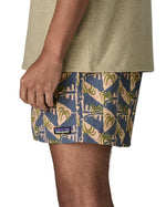 Side of man wearing Patagonia's men's  quick drying baggies shorts with repeating abstract tropical design. Shorts have loose fitting and sit above the knees