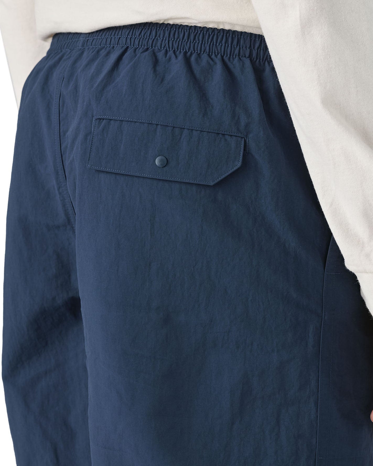 Man wearing Patagonia's men's baggies long 7 in shorts in dark blue. Shows back pocket with popper fastener