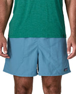 Man wearing Patagonia's men's  quick drying men's baggies shorts in light blue. Shorts have loose fitting and sit above the knees