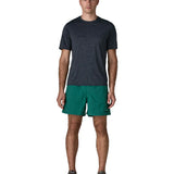 Man wearing Patagonia's men's  quick drying baggies shorts in teal green. Shorts have loose fitting 