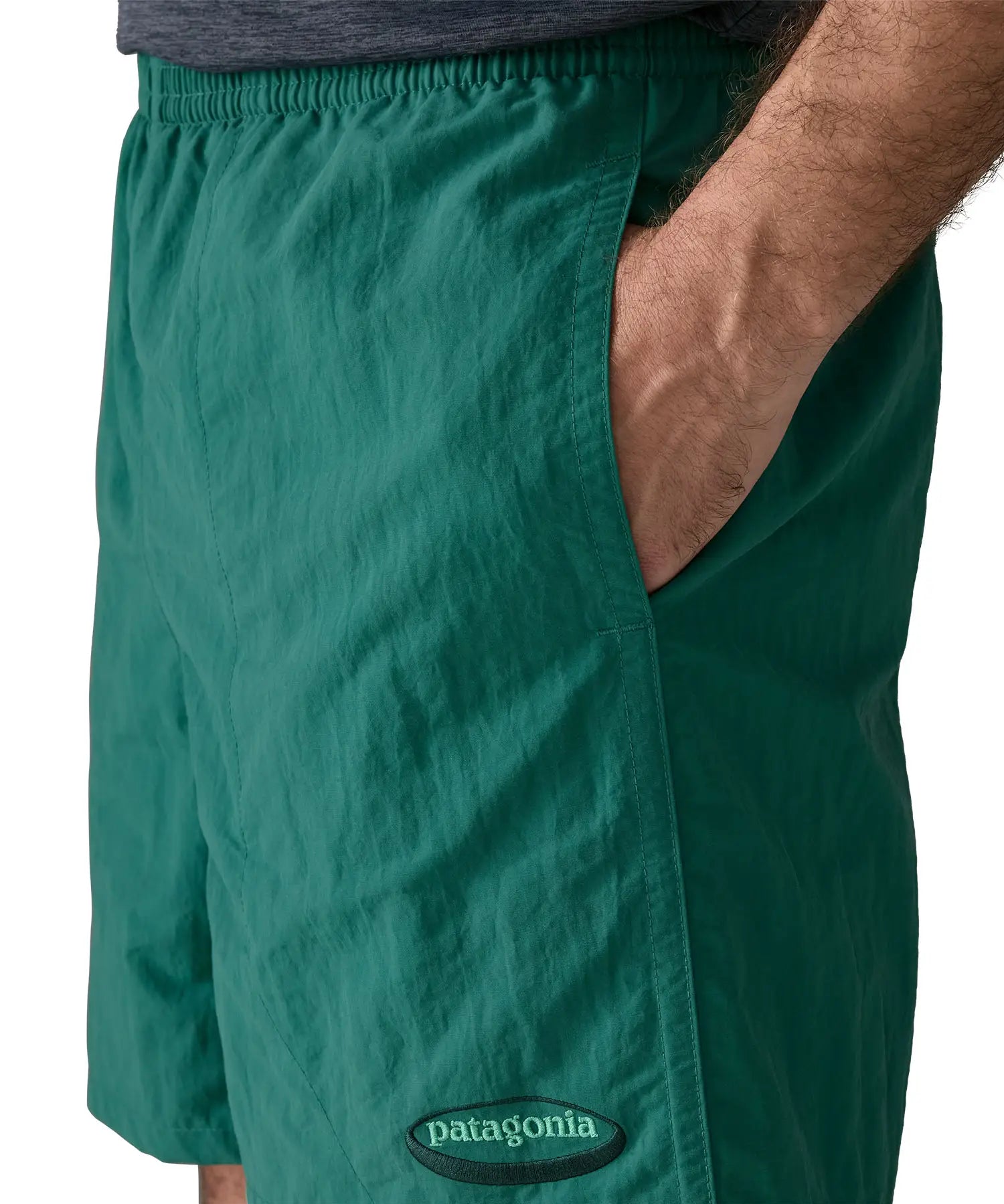Man wearing Patagonias men's quick drying baggies shorts in teal green with hand in side pocket