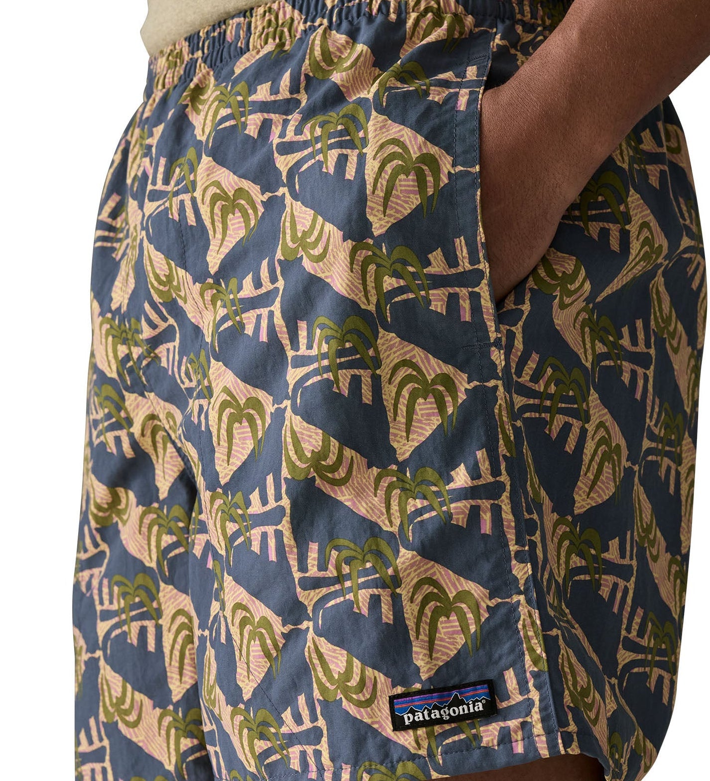 Man wearing Patagonia's men's quick drying baggies shorts with repeating abstract tropical design with hand in side pocket
