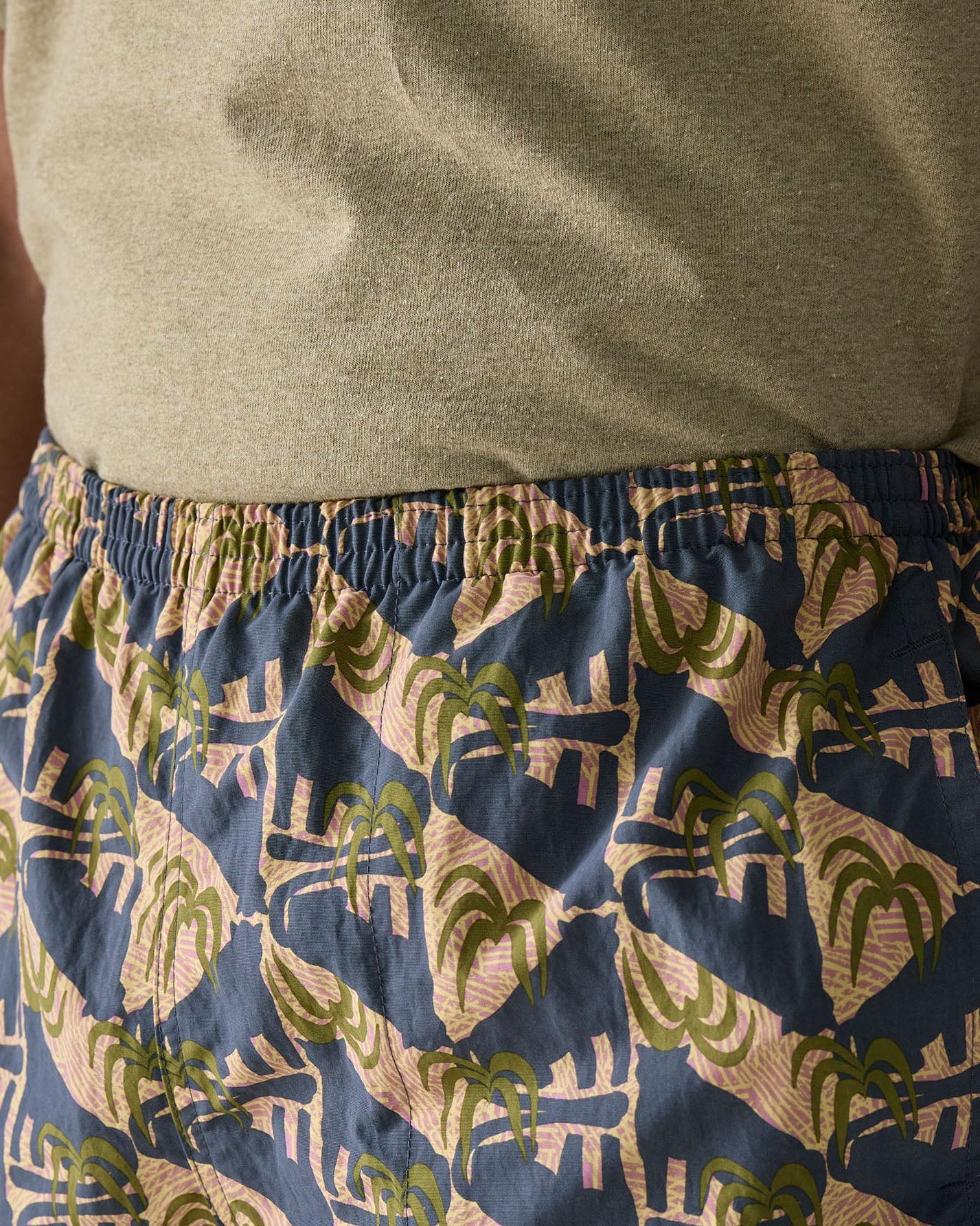 Close up of man wearing Patagonia's men's quick drying baggies shorts with repeating abstract tropical design. Shows elasticated waist band