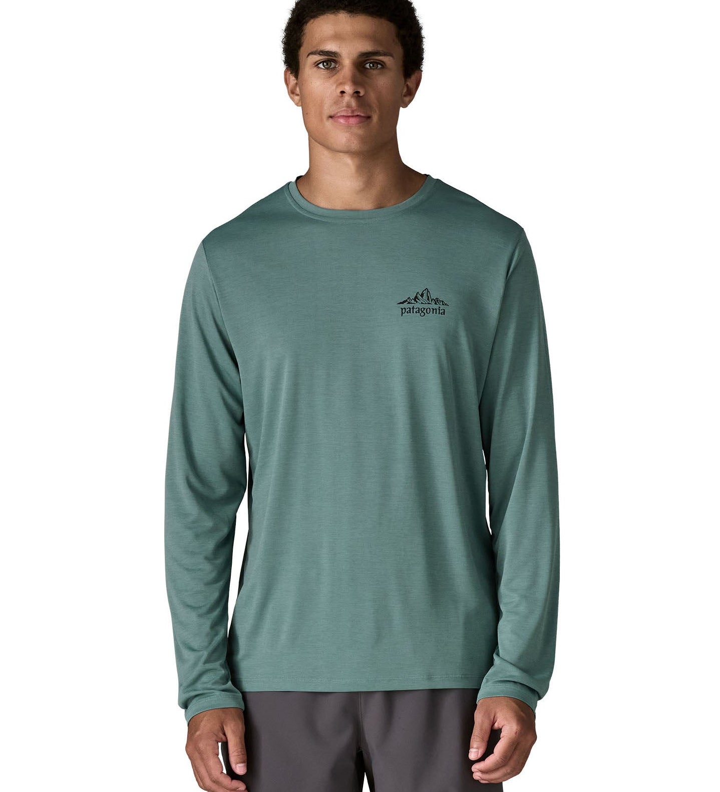 Man wearing Patagonia's men's capilene cool daily long sleeve t-shirt in sage blue with black mountain graphic on upper chest