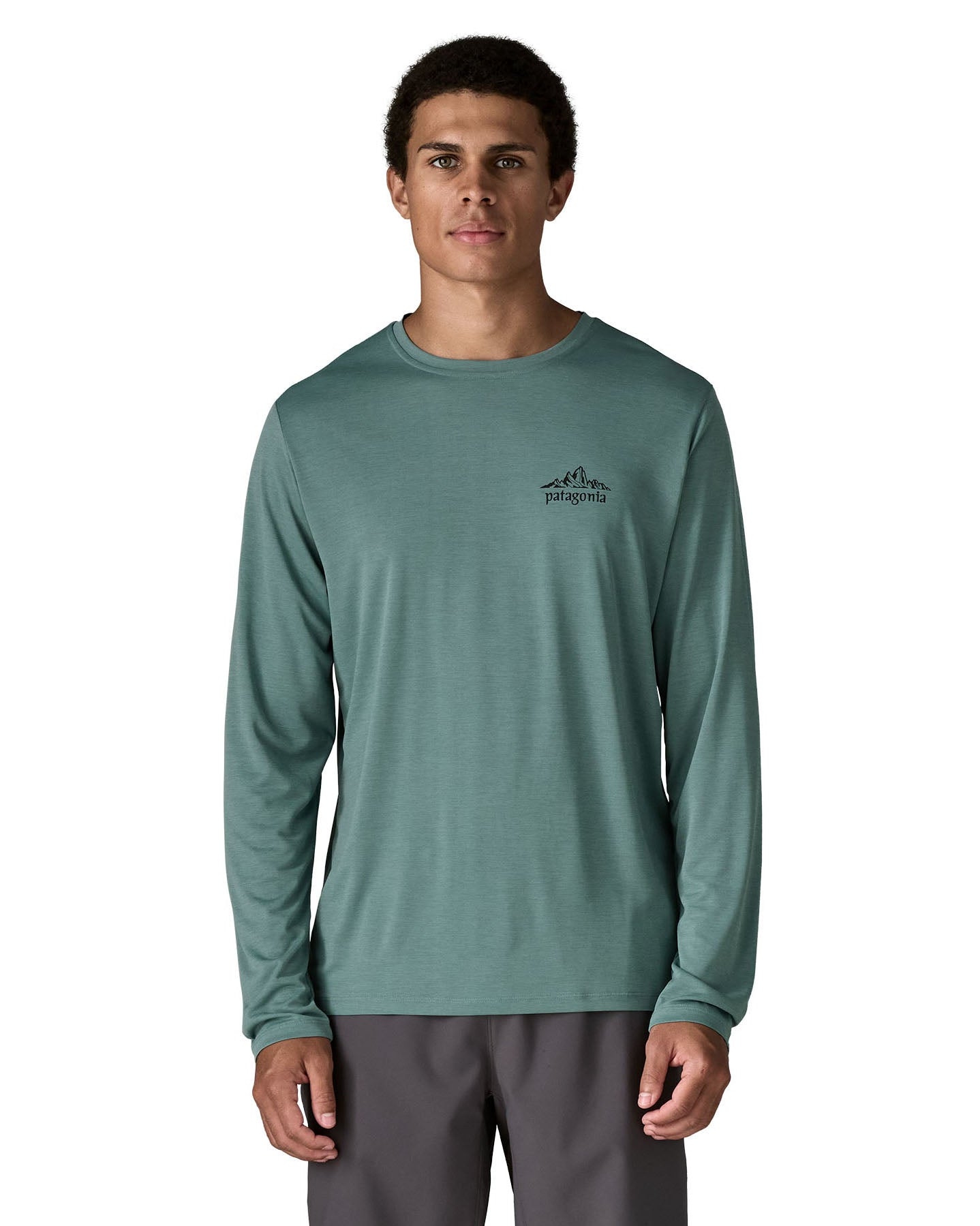 Man wearing Patagonia's men's capilene cool daily long sleeve t-shirt in sage blue with black mountain graphic on upper chest