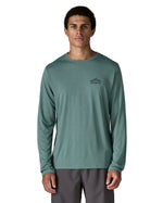 Man wearing Patagonia's men's capilene cool daily long sleeve t-shirt in sage blue with black mountain graphic on upper chest