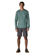Man wearing Patagonia's men's capilene cool daily long sleeve t-shirt in sage blue. T-shirt has a relaxed and sits around the hips