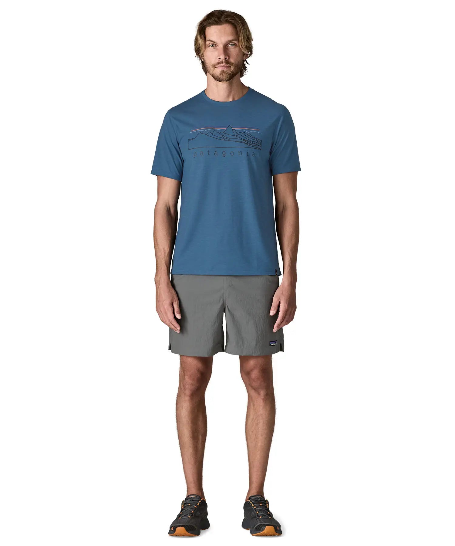 Man wearing Patagonia men's capilene trail short sleeve t-shirt in blue with mountain outline graphic on upper body. T-shirt has a relaxed fit and sits at the hips