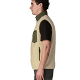 Side of man wearing Patagonia's classic retro x warm fleece vest in beige with green trim showing turned up collar, chest and side pockets
