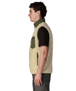 Side of man wearing Patagonia's classic retro x warm fleece vest in beige with green trim showing turned up collar, chest and side pockets
