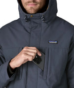 Man putting a mobile phone inside the chest pocket on the Patagonia's isthmus parka jacket in dark blue 