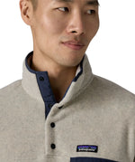 Man wearing Patagonia's lightweight synchilla snap t fleece pullover in beige showing close up of 1/4 length popper fasteners on the front