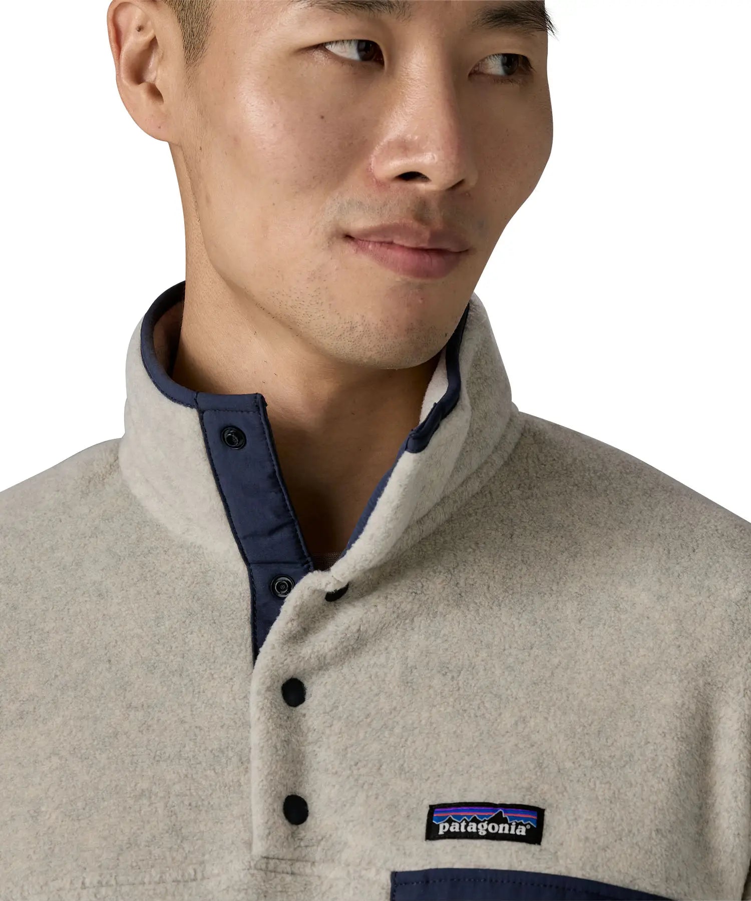 Man wearing Patagonia's lightweight synchilla snap t fleece pullover in beige showing close up of 1/4 length popper fasteners on the front