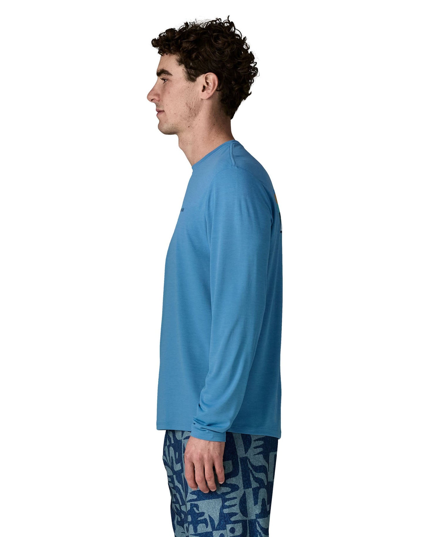 Side of man wearing Patagonia's men's long sleeve capilene cool t-shirt in light blue. T-shirt has a relaxed fit and sits at the hips