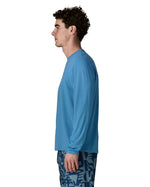 Side of man wearing Patagonia's men's long sleeve capilene cool t-shirt in light blue. T-shirt has a relaxed fit and sits at the hips