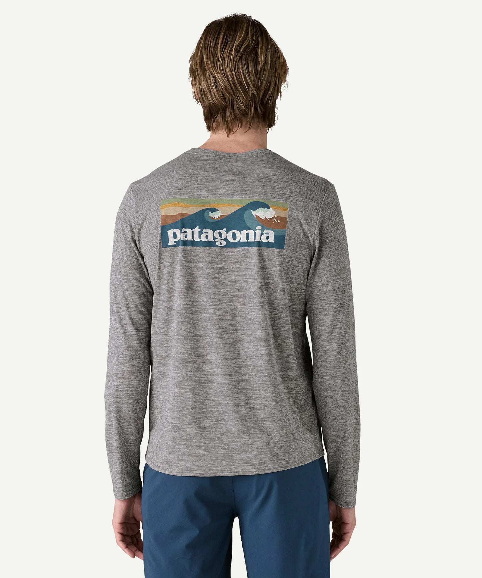 Back view of a man wearing the Patagonia Men’s Long Sleeved Capilene Cool Daily Graphic Shirt in Waters grey marl, featuring the vintage style waves graphic across the upper back.