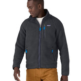 Male in front of a white background wearing brown trousers and a Patagonia thick fleece jacket in black colour with the front zip fastened 