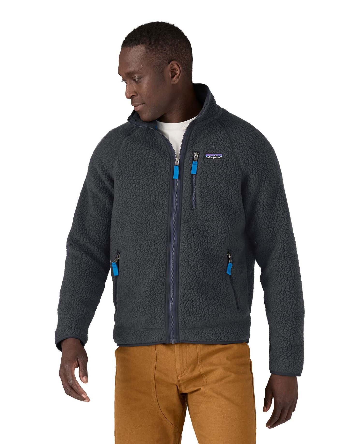 Male in front of a white background wearing brown trousers and a Patagonia thick fleece jacket in black colour with the front zip fastened 