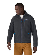 Male in front of a white background wearing brown trousers and a Patagonia thick fleece jacket in black colour with the front zip fastened 