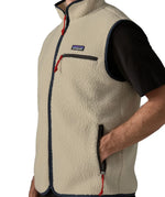 Man wearing Patagonia men's retro pile vest in beige with a navy trim. Showing close up of hand in the side pocket