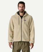 Front three quarter view of a man wearing the Patagonia Men’s Retro-X Fleece Hoody Jacket in Dark Natural, hands in the zippered pockets, showing the full zip and fleece texture.