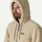 Close up front portrait of a man wearing the Patagonia Men’s Retro-X Fleece Hoody Jacket in Dark Natural with the hood up, showing the thick cream fleece texture and small Patagonia logo.