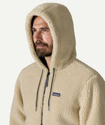 Close up front portrait of a man wearing the Patagonia Men’s Retro-X Fleece Hoody Jacket in Dark Natural with the hood up, showing the thick cream fleece texture and small Patagonia logo.