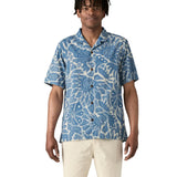 Man wearing Patagonia men's tidal threads camp short sleeve shirt with light blue and cream Hawaiian aloha inspired prints. Shirt has a relaxed fit