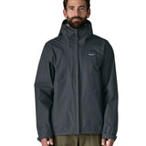Front of man wearing the Patagonia men's waterproof torrentshell 3 layer rain hooded jacket in smolder blue. Jacket has a relaxed fit