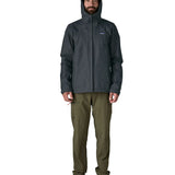 Man wearing the Patagonia men's torrentshell 3 layer rain jacket in smolder blue showing full front zip fastened and hood over the head