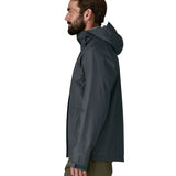 Side of man wearing the Patagonia men's torrentshell 3 layer rain jacket in smolder blue. Jacket has a relaxed fit and sits around the hips 