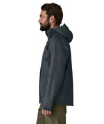 Side of man wearing the Patagonia men's torrentshell 3 layer rain jacket in smolder blue. Jacket has a relaxed fit and sits around the hips 