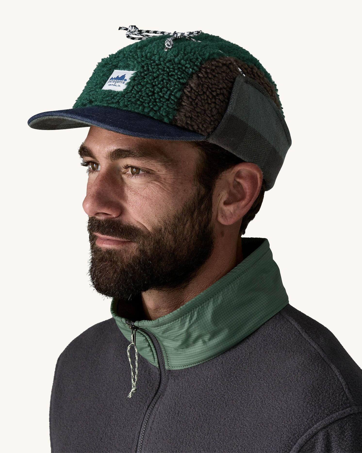 Man wearing Unisex Patagonia Adult Range Earflap Cap in denim, and cascade fleece with flap tied at the top of the head, buy now at Babipur.
