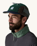 Man wearing Unisex Patagonia Adult Range Earflap Cap in denim, and cascade fleece with flap tied at the top of the head, buy now at Babipur.