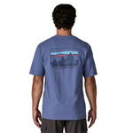 The back of a man wearing the Patagonia Men's 73 Skyline Organic T-Shirt. A blue top with short sleeves with a brand logo in a sketch design printed on the back available at Babipur