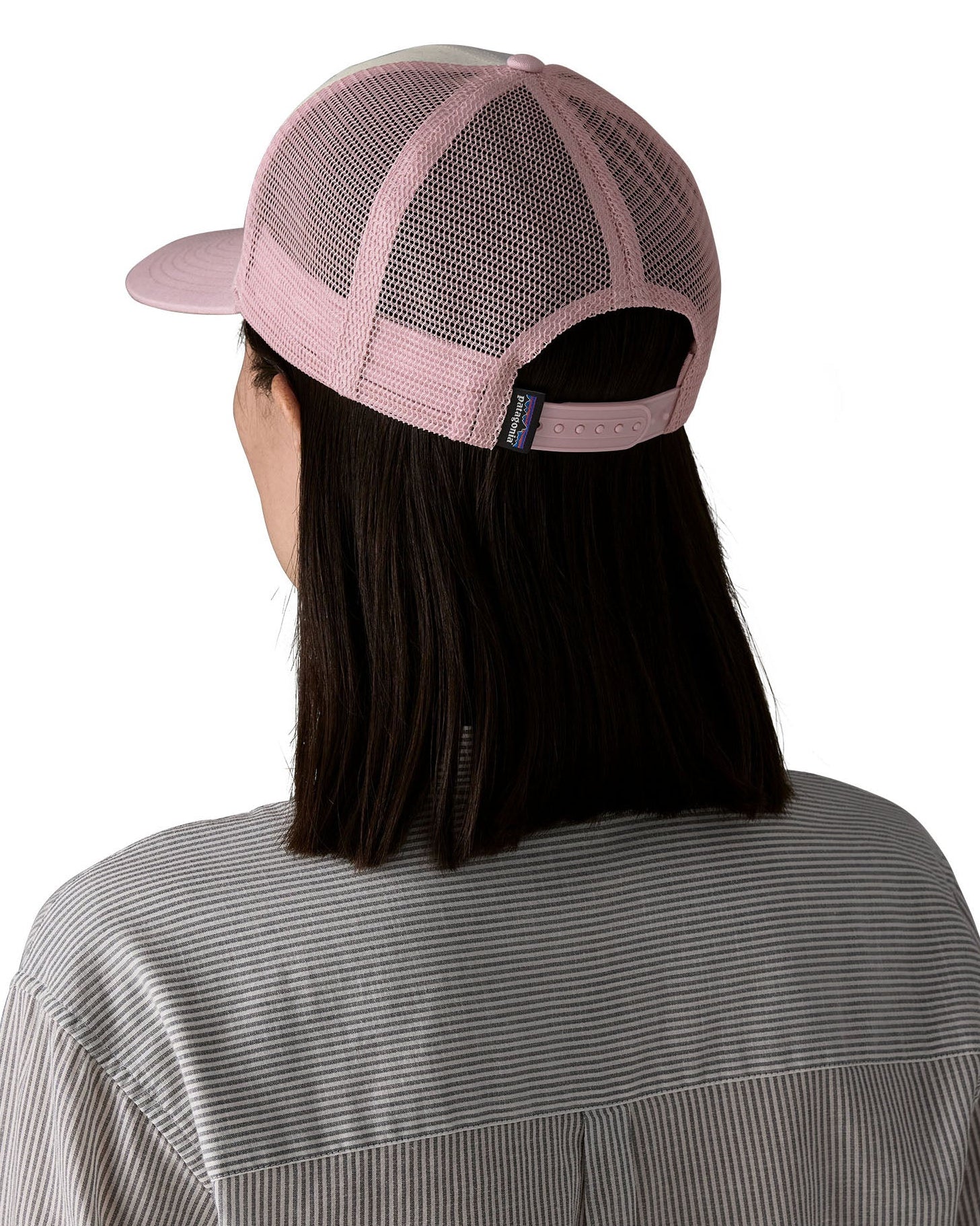 Woman wearing Patagonia's p6 logo trucker hat in white with a pink breathable mesh back panel and adjustable strap
