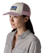 Woman wearing Patagonia's p6 logo trucker hat in white with a pink breathable mesh back panel and visor