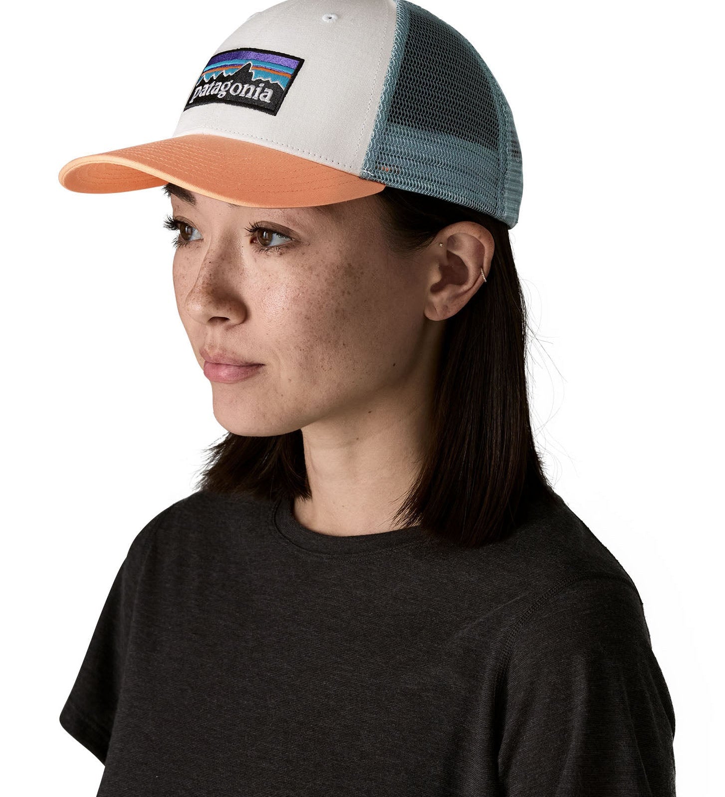 Woman wearing Patagonia's p6 logo lopro trucker hat in white with a breathable blue mesh back panel and orange bill