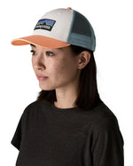 Woman wearing Patagonia's p6 logo lopro trucker hat in white with a breathable blue mesh back panel and orange bill