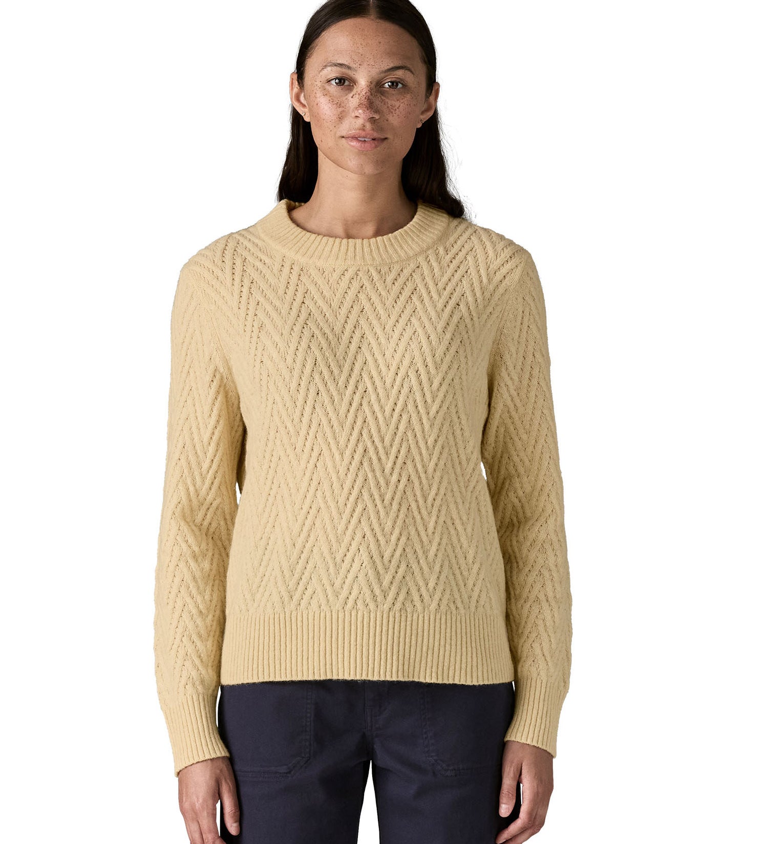 A woman wearing the Patagonia Women's Recycled Wool-Blend Crewneck Sweater - in dark natural colour available at Babipur.. A heavy knitted  jumper with a chevron style design 