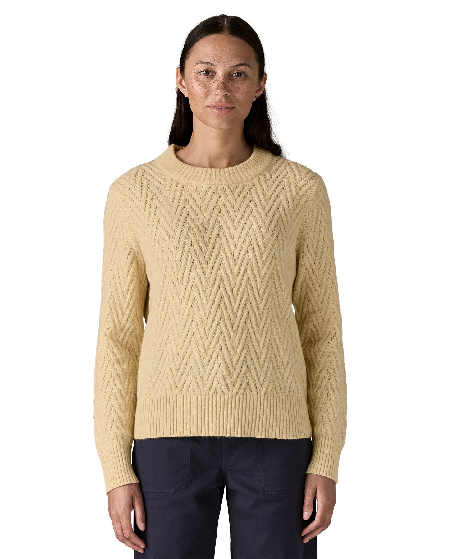 A woman wearing the Patagonia Women's Recycled Wool-Blend Crewneck Sweater - in dark natural colour available at Babipur.. A heavy knitted  jumper with a chevron style design 