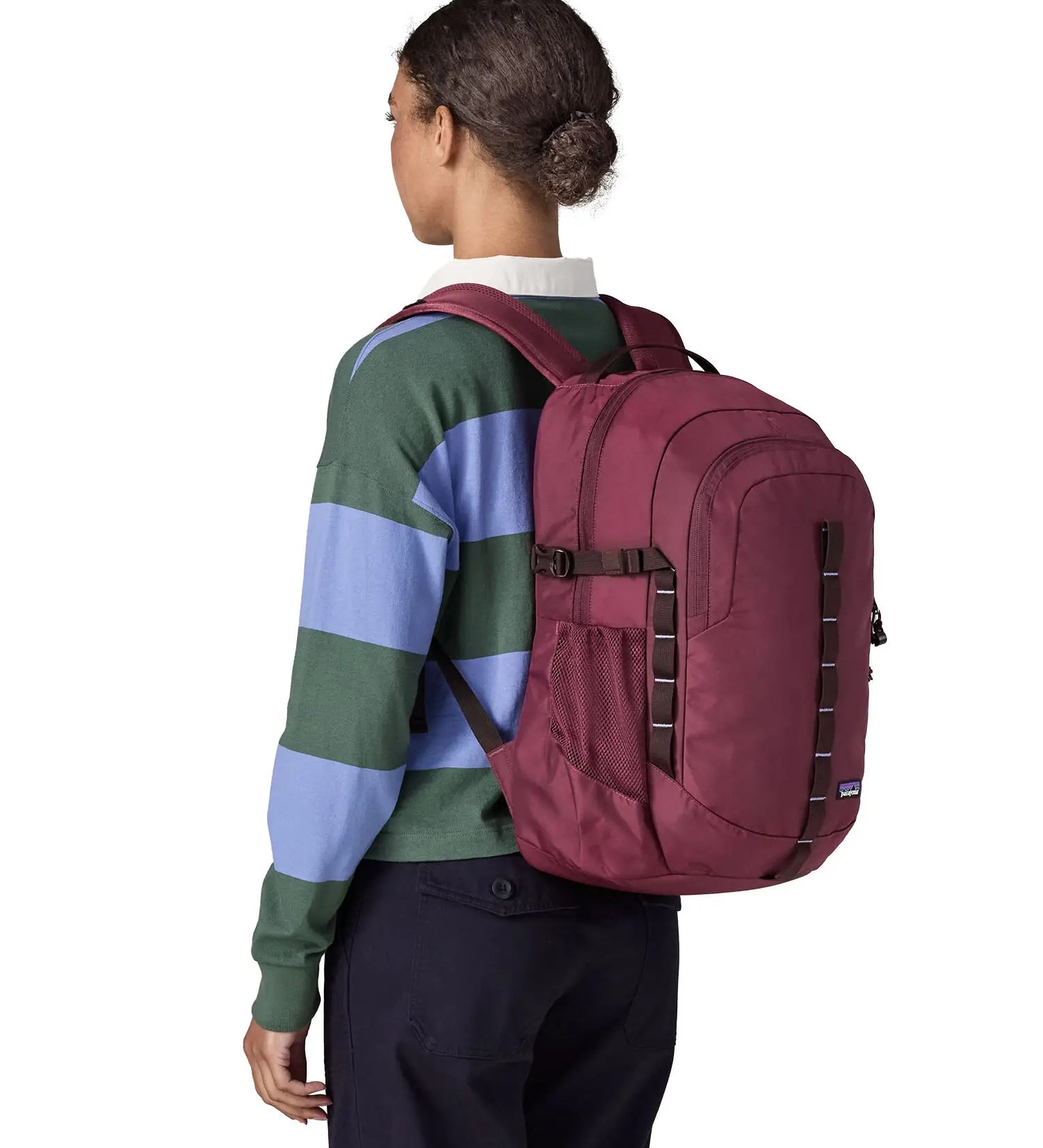 Back of woman carrying a Patagonia's 30L refugio backpack in maroon on the shoulders showing mesh side pockets and brown gear loops
