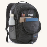 Patagonia refugio backpack in black with open front compartment with stationery placed inside and a bottle in the side holder.