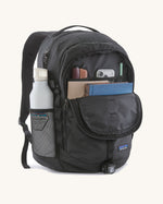 Patagonia refugio backpack in black with open front compartment with stationery placed inside and a bottle in the side holder.