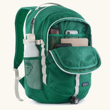 Patagonia 26L refugio backpack in green with open front compartment with stationery placed inside and a bottle in the side holder.