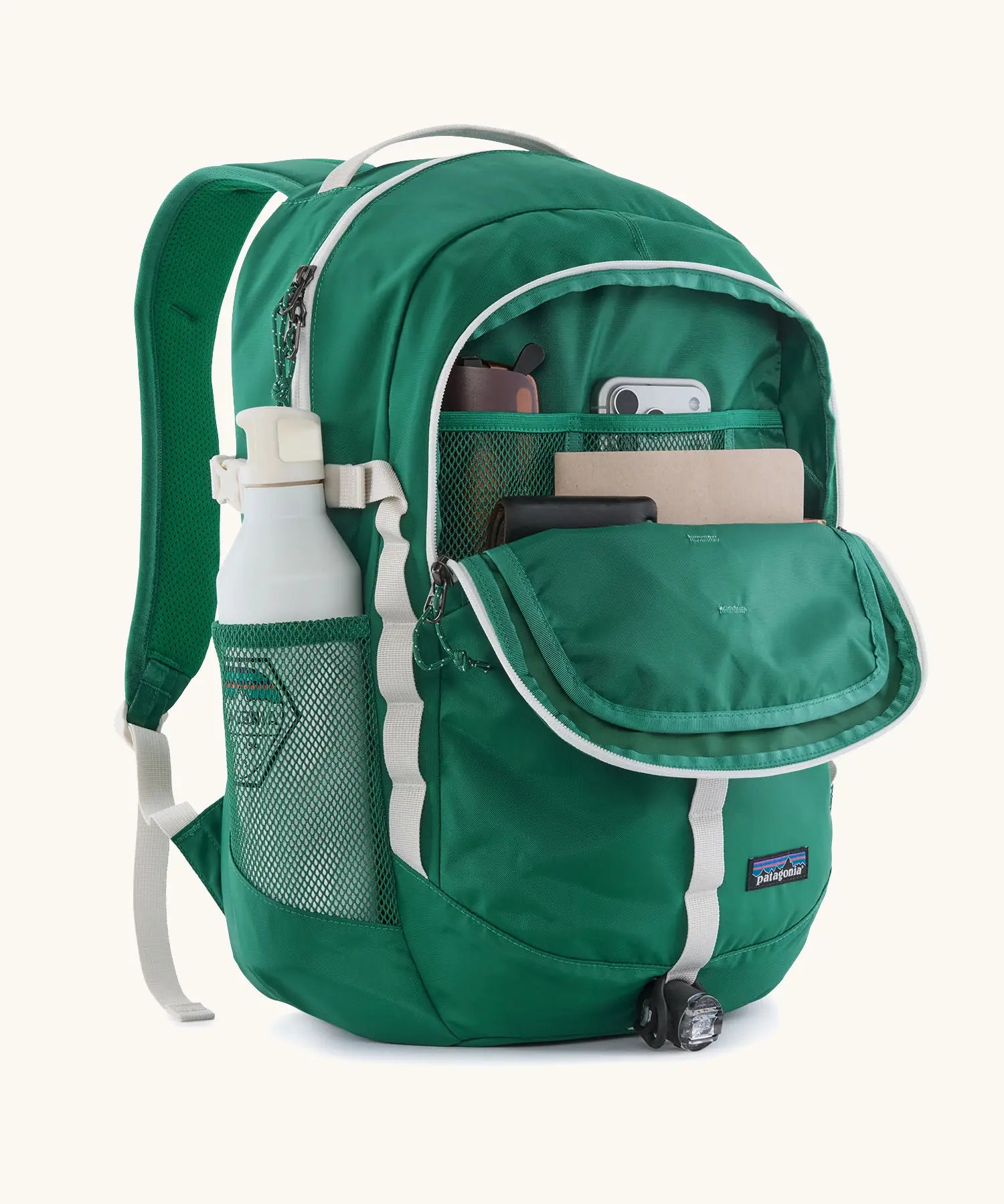 Patagonia 26L refugio backpack in green with open front compartment with stationery placed inside and a bottle in the side holder.
