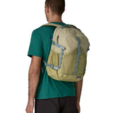 Man wearing Patagonia's 30L refugio backpack in light green with side bottle holder and grey gear loops and quick release buckles.