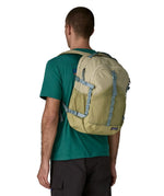 Man wearing Patagonia's 30L refugio backpack in light green with side bottle holder and grey gear loops and quick release buckles.