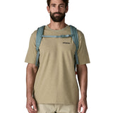 Man wearing Patagonia's refugio 32L daypack in sage blue. Shows shows front buckle fastened